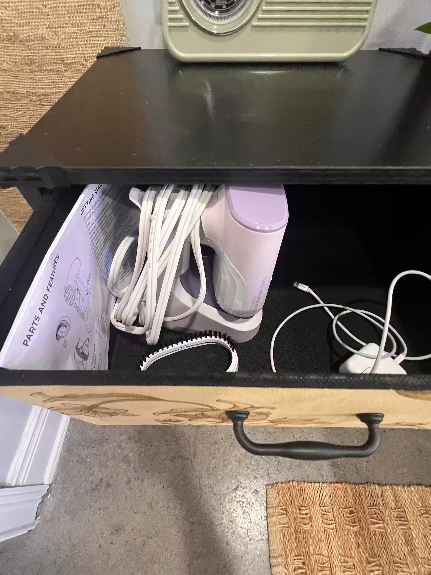 Un cajón con un manual, cables blancos y un dispositivo rosa.