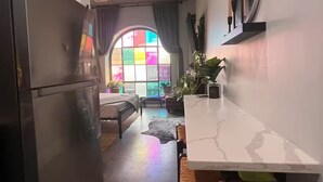A kitchen with a refrigerator, a dining area with a white marble countertop, and a window with colorful panes.