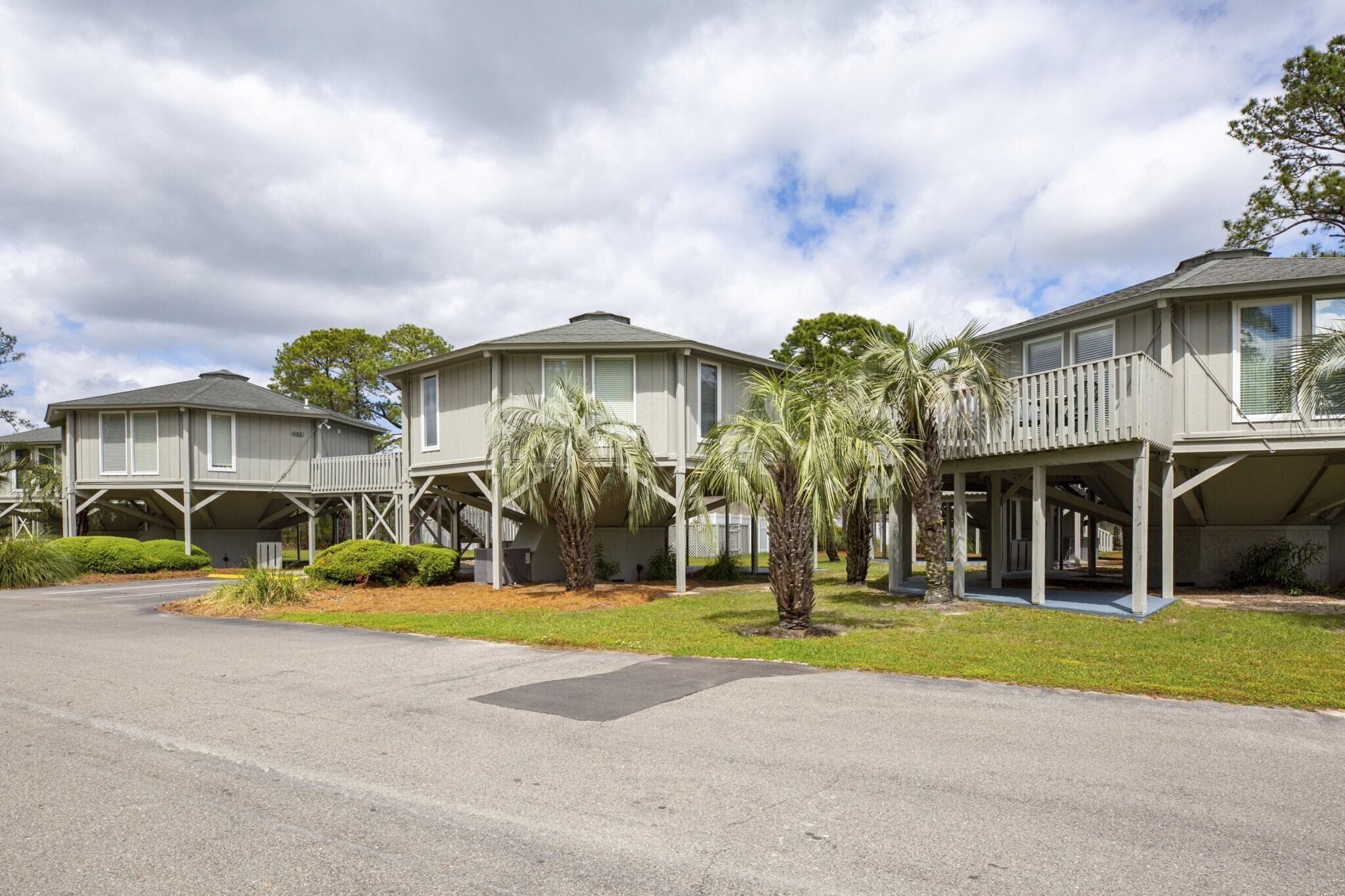 A row of two-story houses with attached porches, surrounded by well-maintained lawns and palm trees.