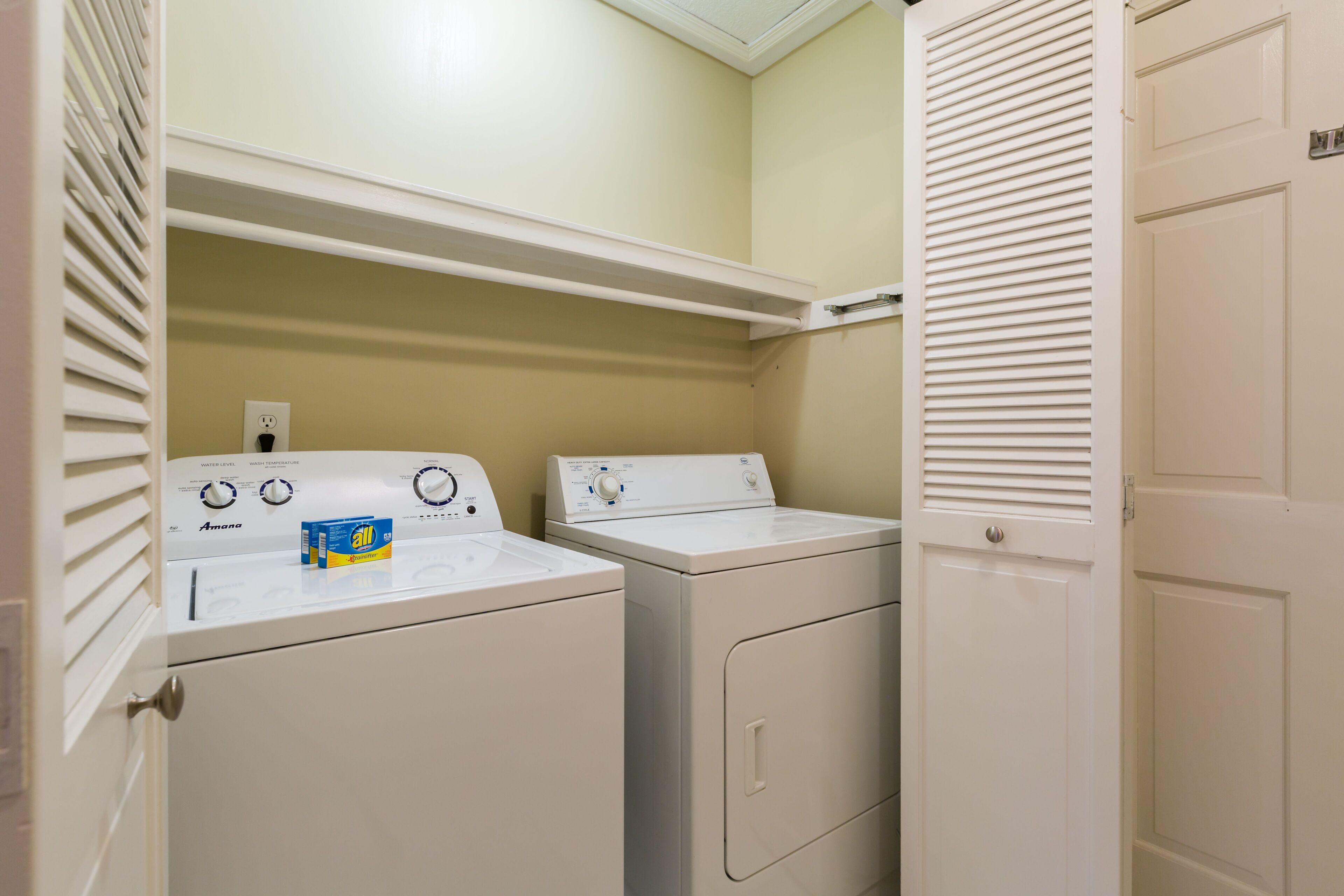 A laundry room with two stacked washers and dryers, a shelf above, and a door on the right.