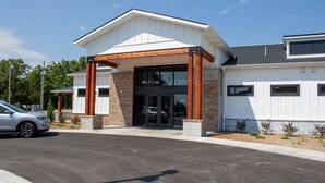 A modern building with a covered entrance, a parking lot, and a car parked in front. - 1BR Suite w/ Kitchen & Balcony Access (Branson)