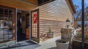 A log cabin with a wooden exterior, a glass door entrance, and a stone planter with a tree. - Serene 4-BR Lodge w/ Pools & Patio (Branson)