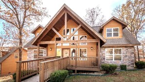 A two-story lodge with a wooden deck, stone exterior, and a covered entrance. - Serene 4-BR Lodge w/ Pools & Patio (Branson)