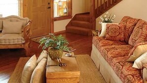 A spacious living room with a high ceiling, wooden beams, a staircase, and large windows. - Serene 4-BR Lodge w/ Pools & Patio (Branson)