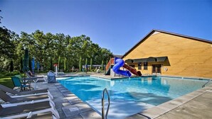 A swimming pool with a slide, lounge chairs, and a wooden building in the background. - Serene 4-BR Lodge w/ Pools & Patio (Branson)