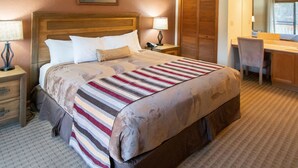 A hotel room with a large bed, a desk with a chair, a lamp, and a mirror.