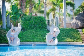 Two people sliding down a water slide into a pool surrounded by palm trees and greenery. - 2BR Villa with Pool Access near Disney (Kissimmee)