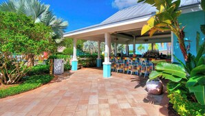 A covered outdoor area with a tiled floor, a bar with chairs, and lush tropical plants.