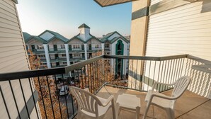 Un balcon avec deux chaises en plastique blanches et une table, donnant sur un parking et des bâtiments dotés de toits végétalisés.