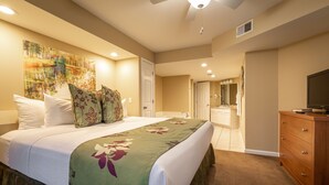 A hotel room with a large bed, a ceiling fan, a bathroom with a mirror, and a wooden dresser.