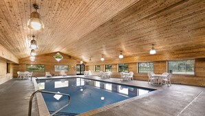En indendørs swimmingpool med trævægge og -loft, omgivet af hvide stole og borde.