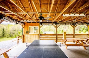 A wooden cabin with a dining area, a ceiling fan, and a view of the forest.