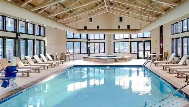 An indoor swimming pool with lounge chairs and a hot tub.