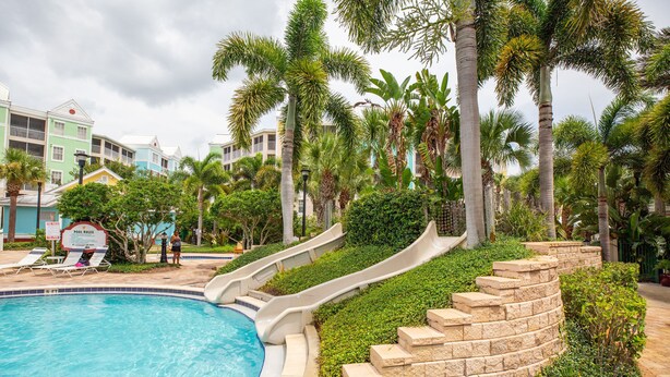 A swimming pool with a slide, surrounded by palm trees and a sign indicating pool rules. - 1BR Villa near Disney & Universal (Kissimmee)