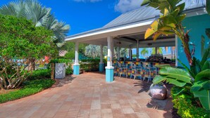 A covered outdoor seating area with a tiled floor, surrounded by greenery and a building with a blue exterior. - 1BR Villa near Disney & Universal (Kissimmee)