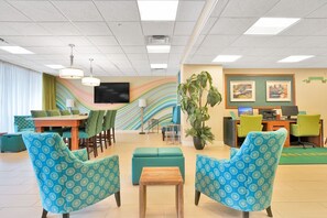 A lobby with a reception desk, a television, a large plant, and seating areas.