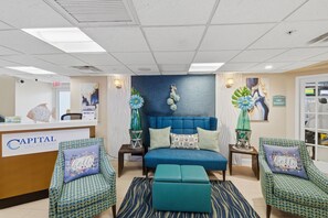 A hotel lobby with a reception desk, a blue upholstered sofa, two patterned armchairs, and a decorative wall. - Studio at Hollywood Beach w/ Pools & Boardwalk (Hollywood)