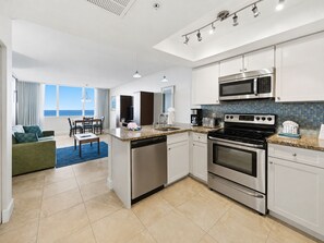 A modern kitchen with stainless steel appliances, a dining area with a view, and a living room with a sofa and a TV. - Oceanfront Studio w/ Pool in Hollywood Beach (Hollywood)