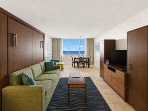 A modern hotel room with a sofa, dining table, and a TV.