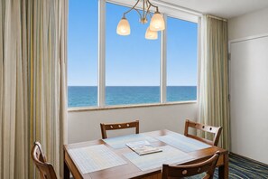 Un comedor con vista al océano, una mesa de madera, cuatro sillas y una lámpara colgante.