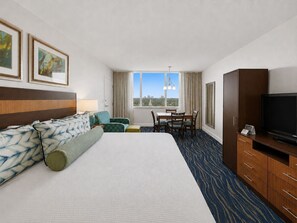 Habitación de hotel con una cama grande, un escritorio con sillas, televisión y vista a la ciudad.