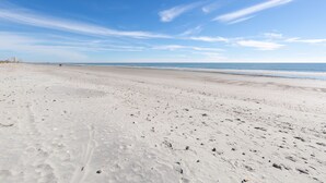 Una amplia playa de arena con huellas y un cielo azul despejado.