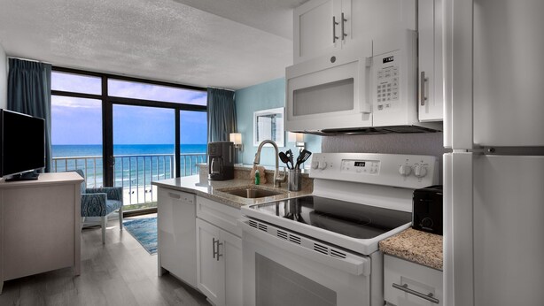 Una cocina moderna con vista al océano, muebles blancos, horno empotrado y cafetera.