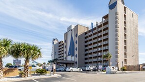 A multi-story hotel with a distinctive sailboat logo, a pool, and a beach club sign.