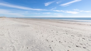 A wide sandy beach with footprints and a clear blue sky.