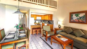 A spacious living area with a dining table, two bar stools, a sofa, and a kitchen in the background.