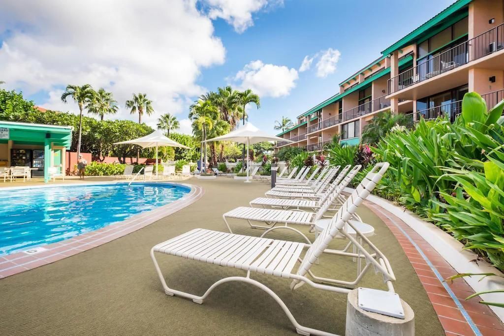 A hotel pool area with sun loungers, a swimming pool, and a building with balconies.
