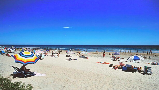 A beach with umbrellas, sun loungers, and people relaxing.