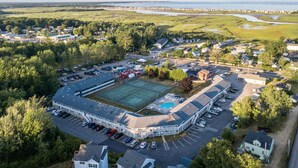 An aerial view of a large sports complex with a tennis court, parking area, and surrounding buildings.