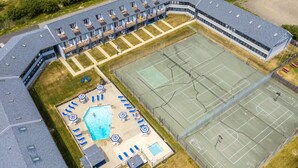 An aerial view of a building with a swimming pool, tennis courts, and a covered outdoor seating area.