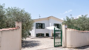 A white building with green shutters, a gated entrance, and a stone-paved courtyard.