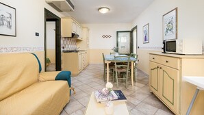 A compact living space with a sofa, dining table, chairs, a kitchenette, and a microwave.