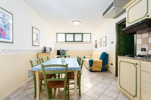 Un coin repas avec une table et des chaises, un canapé, une cuisine équipée d’armoires et une fenêtre avec des stores.