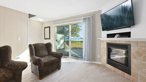 Una sala de estar con chimenea, televisor y vistas a una terraza y árboles.