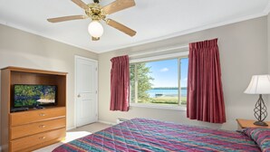 Un dormitorio con una cama grande, un ventilador de techo, un televisor sobre un mueble de madera y una ventana con cortinas.