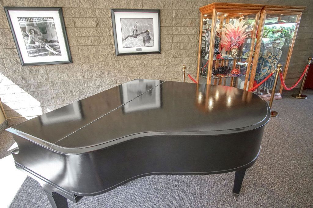 Un piano noir dans une pièce dont les murs sont ornés de tableaux encadrés, et une vitrine contenant des objets décoratifs.