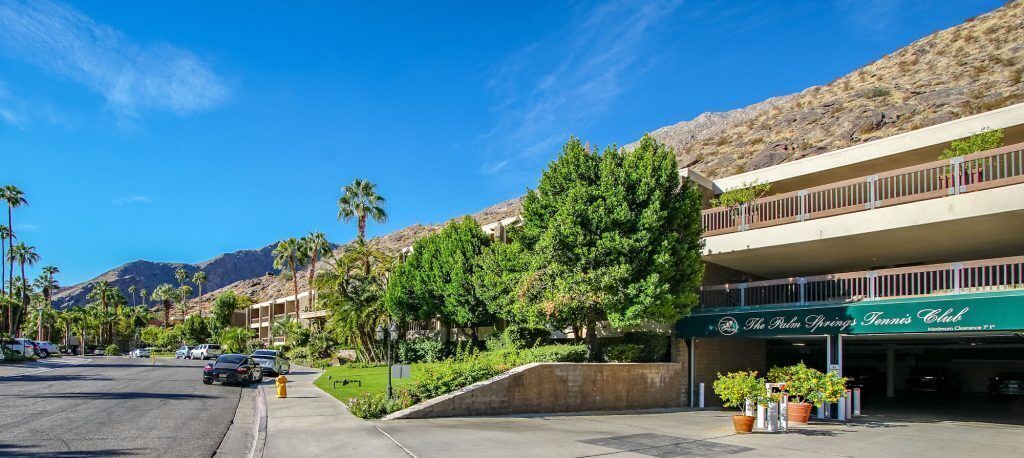A hotel with a green sign, a parking lot, and a mountain in the background.