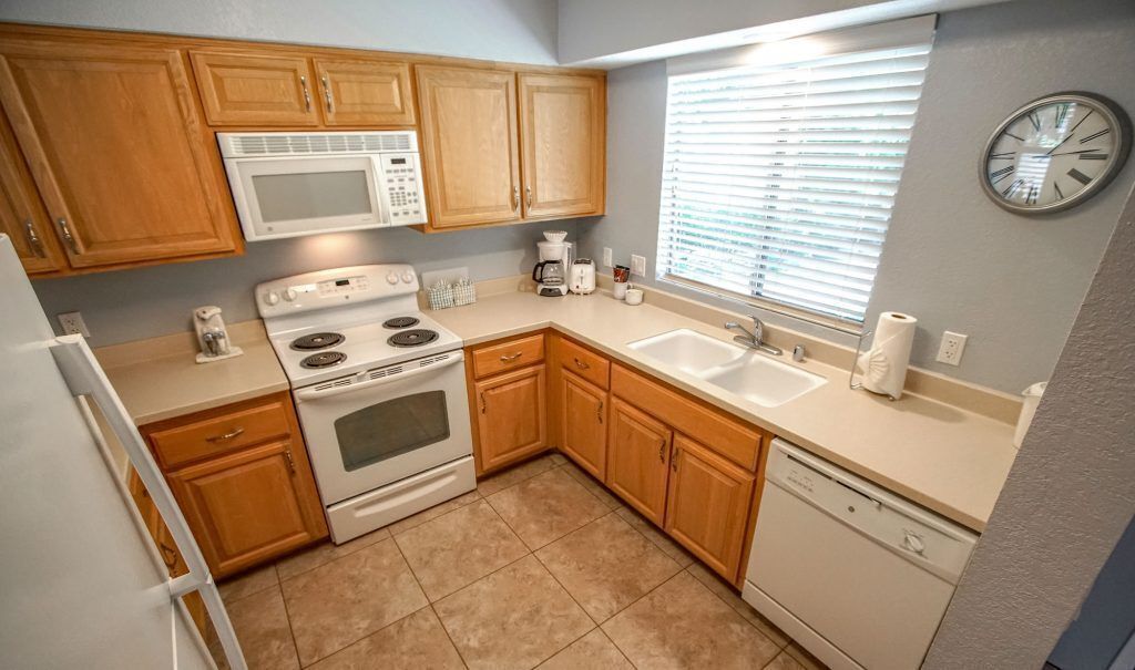 A compact kitchen with wooden cabinets, a microwave, stove, sink, and dishwasher.