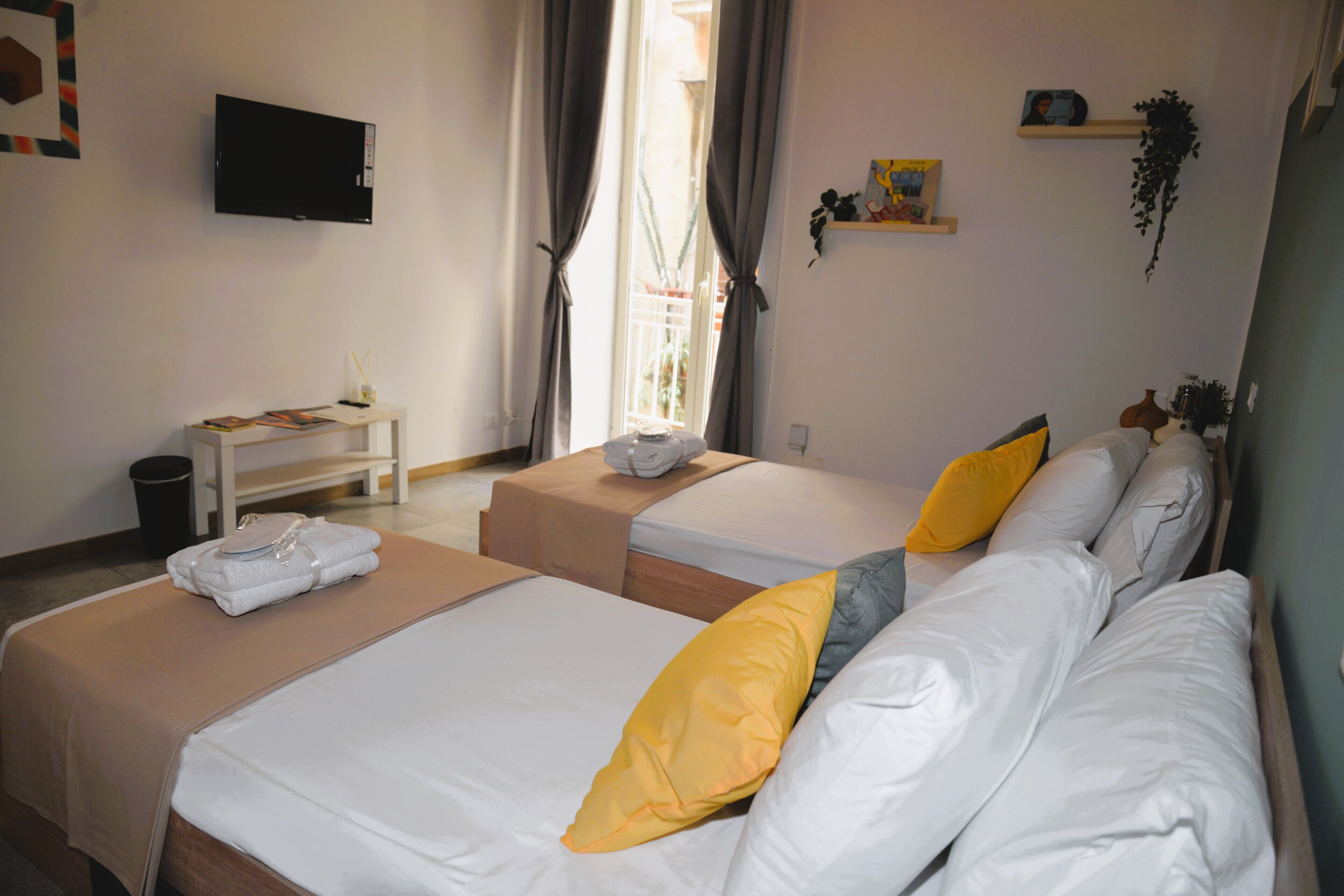 A hotel room with two beds, a TV, a desk, and a window with curtains.