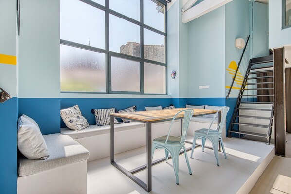 Una habitación con ventana, una mesa, sillas, un banco y una escalera.