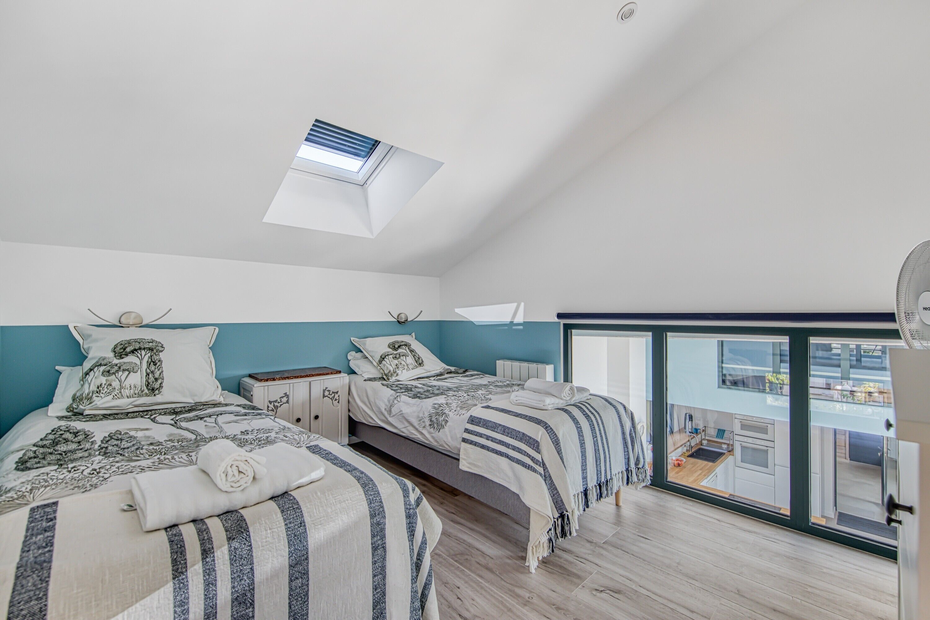 A bedroom with two beds, a skylight, a view to the outside, and a small kitchenette.