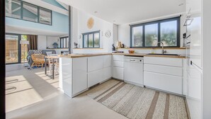 Una cocina moderna con armarios blancos, un ventanal grande y un comedor con mesa y sillas.