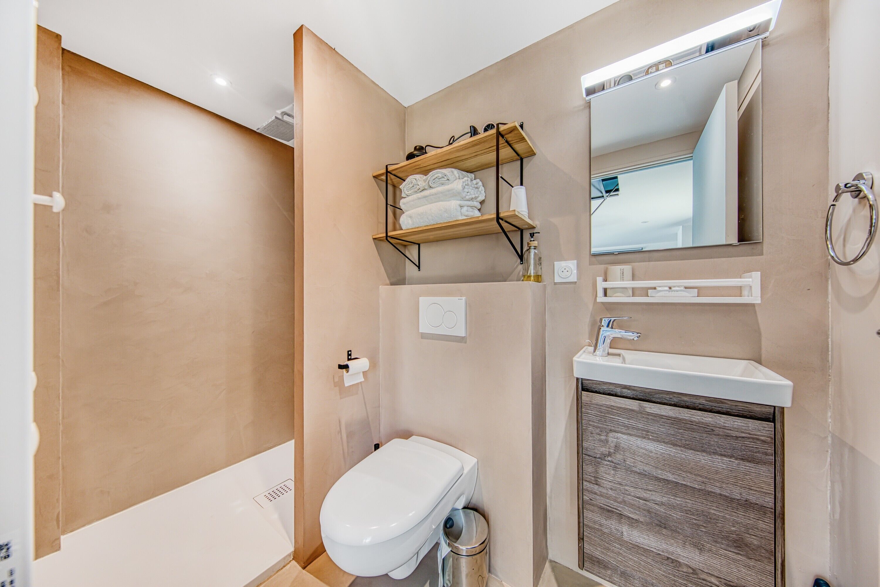 A bathroom with a toilet, sink, mirror, towel rack, and shower area.