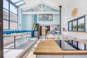 Un interior moderno con techo alto, una escalera que conduce a un nivel superior y un comedor con mesas y sillas.