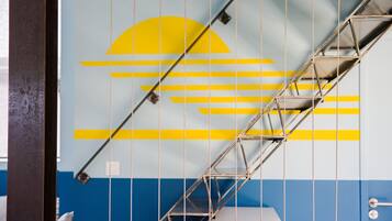 A metal staircase with a geometric design, a blue and yellow wall with a sun motif, and a white object at the bottom.