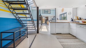 Una cocina moderna con armarios blancos, una isla central y una escalera con barandillas de vidrio.